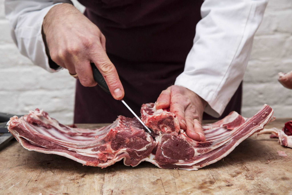A butcher using a sharp knife to prepare lamb ribs for rack of lamb. ,Butcher's Shop
